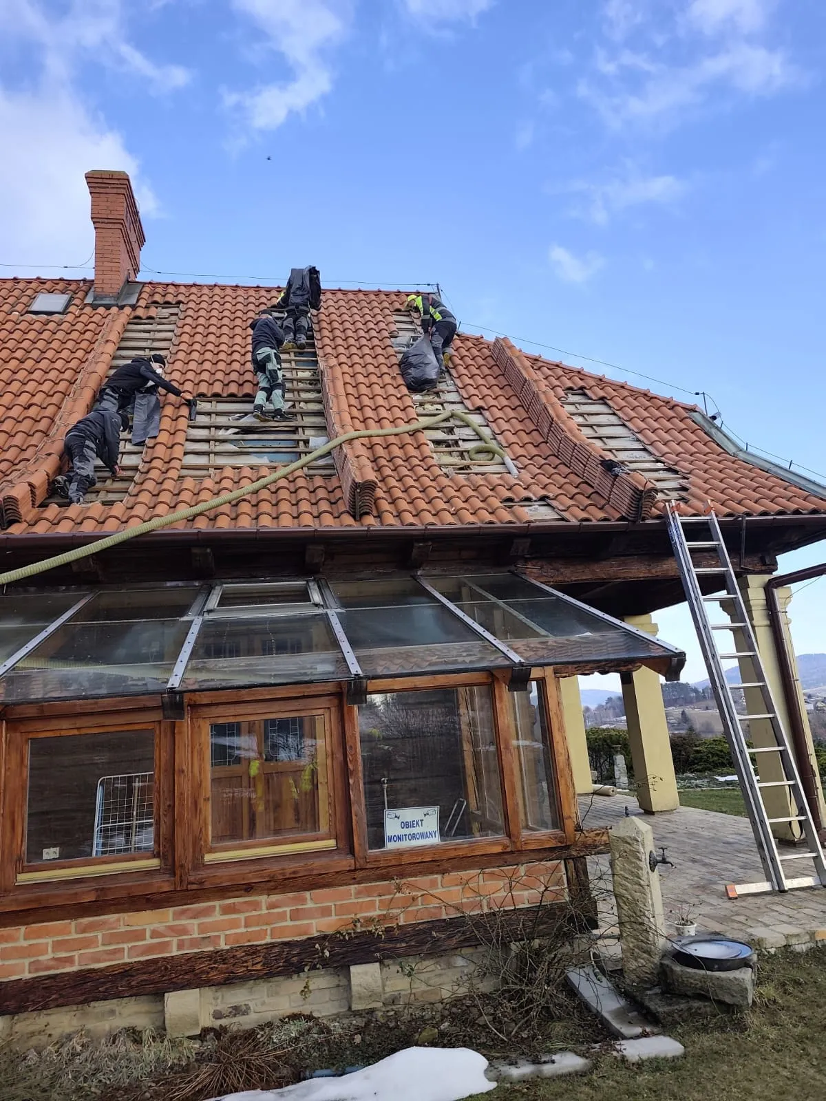 Ekipa System Term pracująca na dachu dużego, tradycyjnego domu z oranżerią