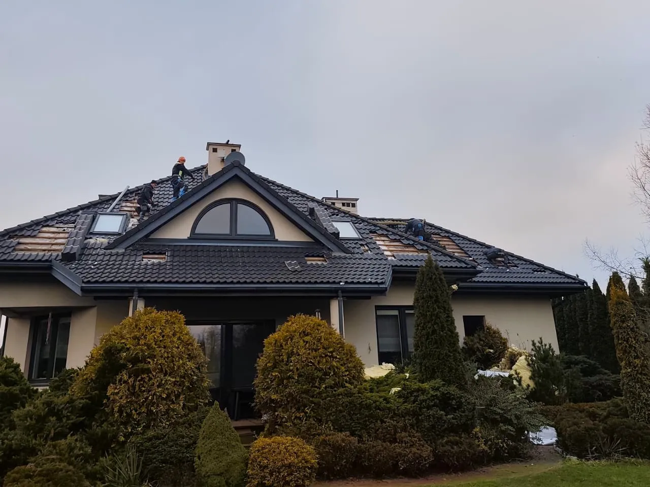 Elegancki dom z ekipą pracującą na dachu w pochmurny dzień