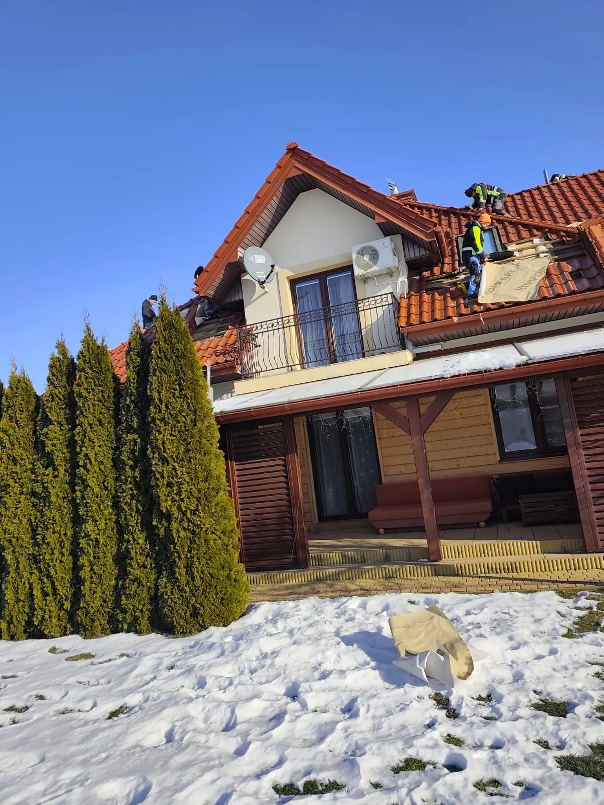Docieplanie dachu zimą — ekipa na dachu domu ze śniegiem na ziemi