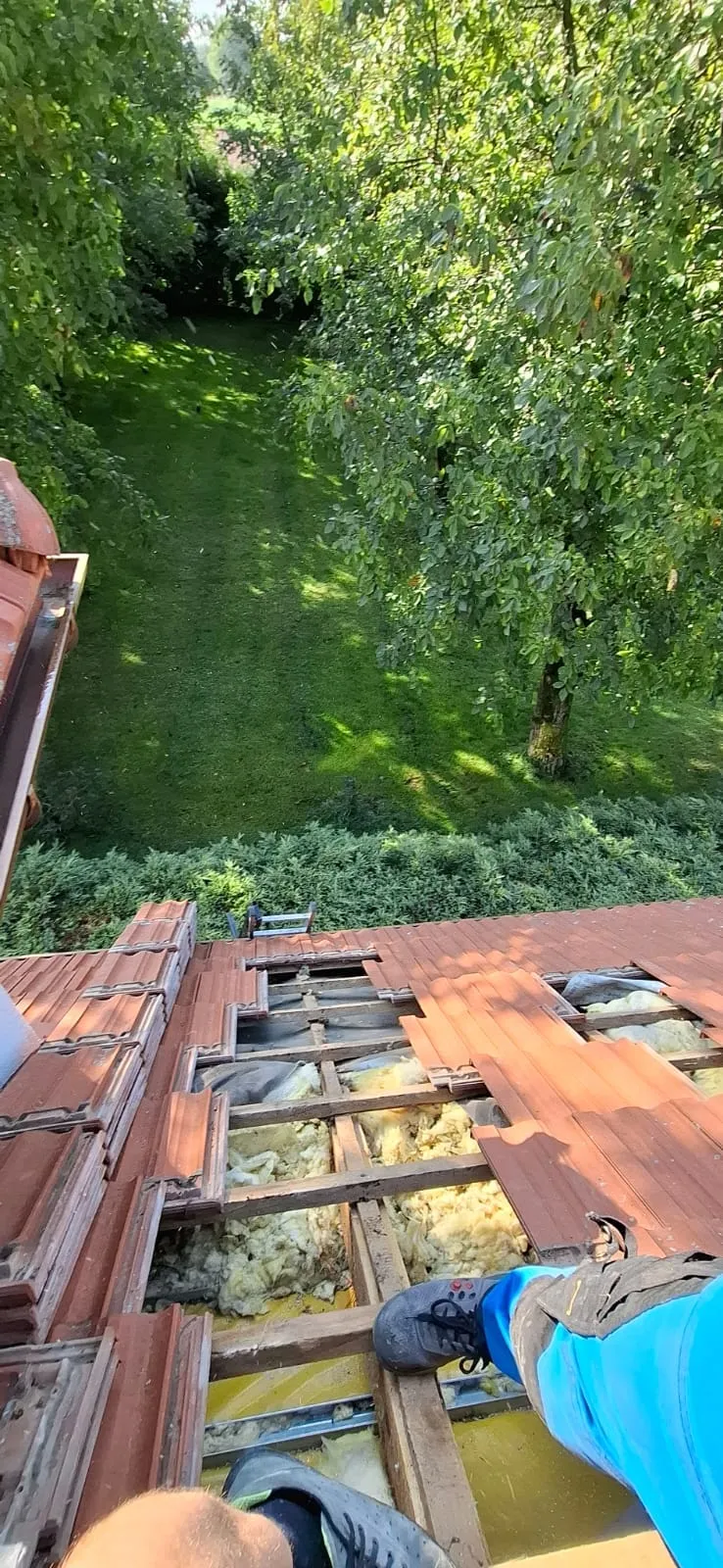 Zdjęte dachówki odsłaniające warstwę izolacji nad zielonym ogrodem