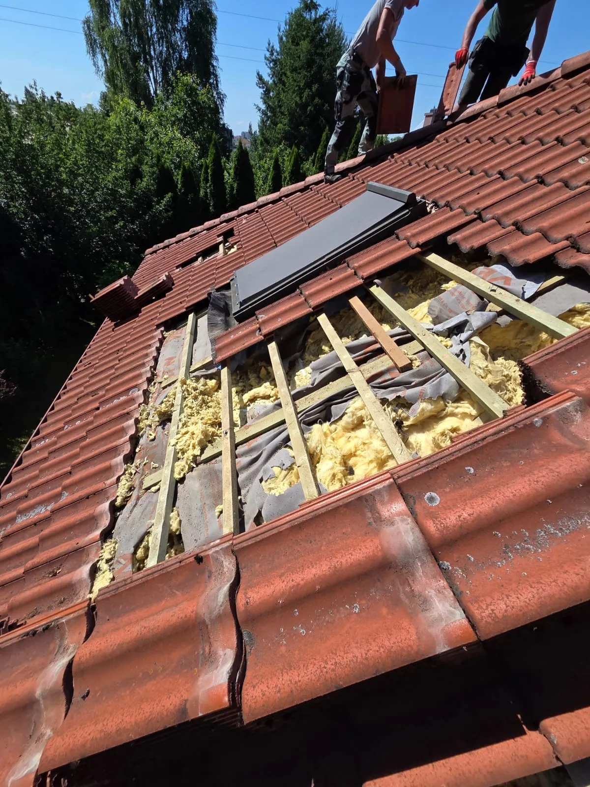 Dwóch pracowników zdejmujących dachówki podczas przygotowania do wymiany izolacji